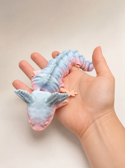Pastel articulated axolotl resting in an adult woman hand for scale