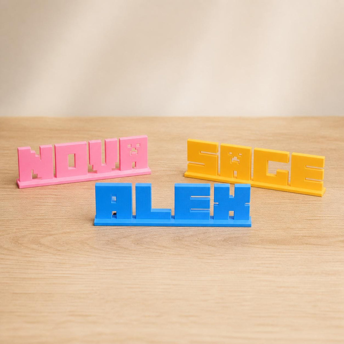 Nova, Alex and Sage block letter personalised PLA nameplates arranged in a warm neutral studio setting.