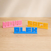 Nova, Alex and Sage block letter personalised PLA nameplates arranged in a warm neutral studio setting.