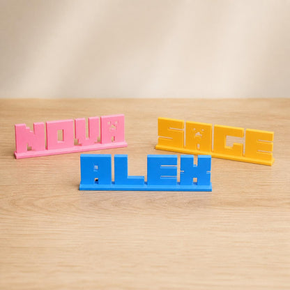 Nova, Alex and Sage block letter personalised PLA nameplates arranged in a warm neutral studio setting.