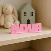 Nova block letter personalised nameplate displayed on a warm neutral nursery shelf.