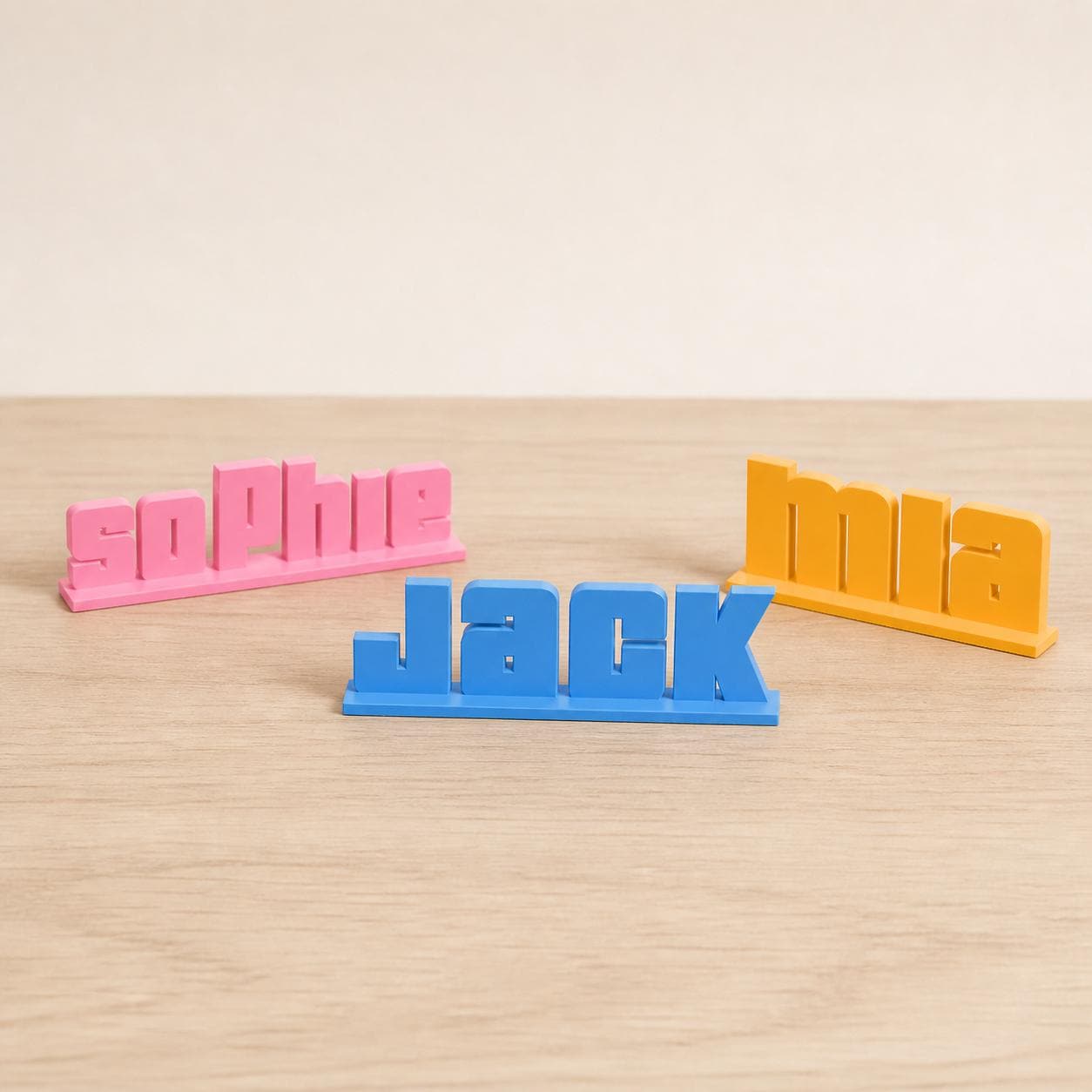 Sophie, Jack and Mia bold arcade personalised PLA nameplates arranged in a warm neutral studio setting.
