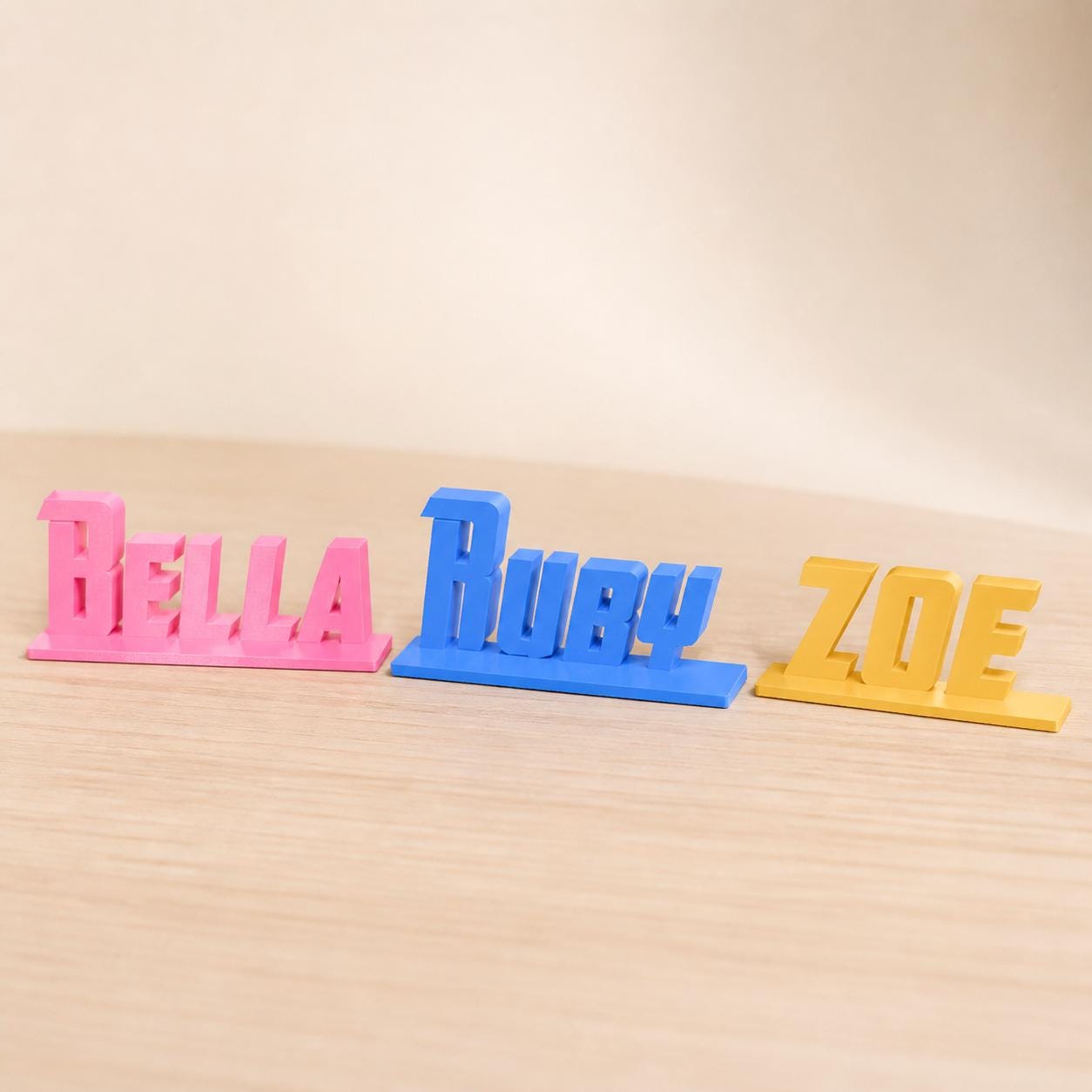Bella, Ruby and Zoe heroic angular personalised PLA nameplates arranged in a warm neutral studio setting.