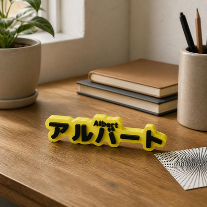 Virtual lifestyle scene of the yellow and black Albert and アルバート personalised nameplate standing upright on a natural wood home-study desk.