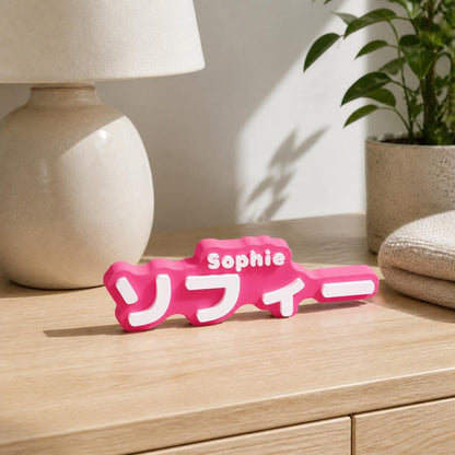Virtual lifestyle scene of the magenta and white Sophie and ソフィー personalised nameplate standing on a pale wood bedroom dresser.