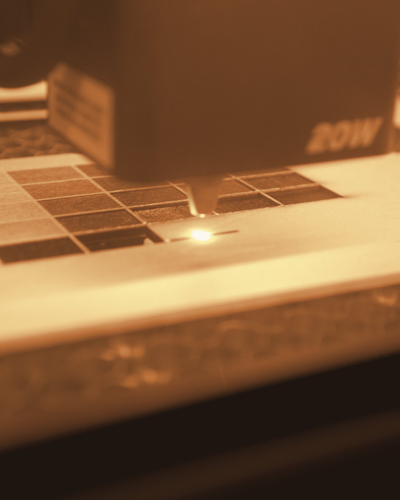 A 20 watt laser cutting a sheet of birch plywood, seen through the amber safety window